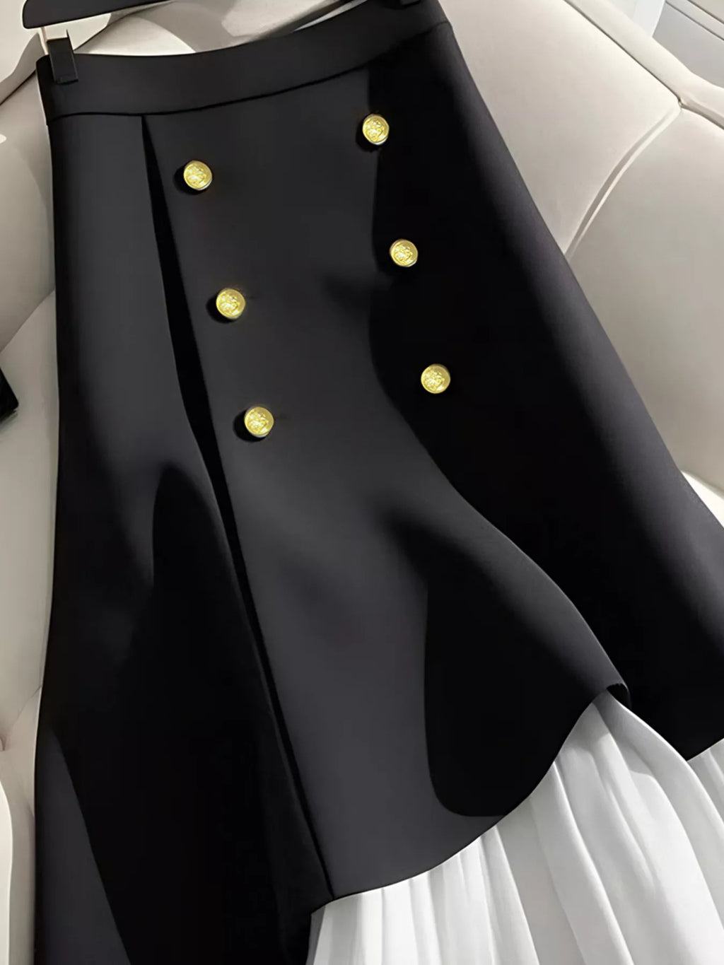 "Jupe plissée noire taille haute avec détails boutonnés - vue de face montrant les plis élégants et la structure architecturale BLACK