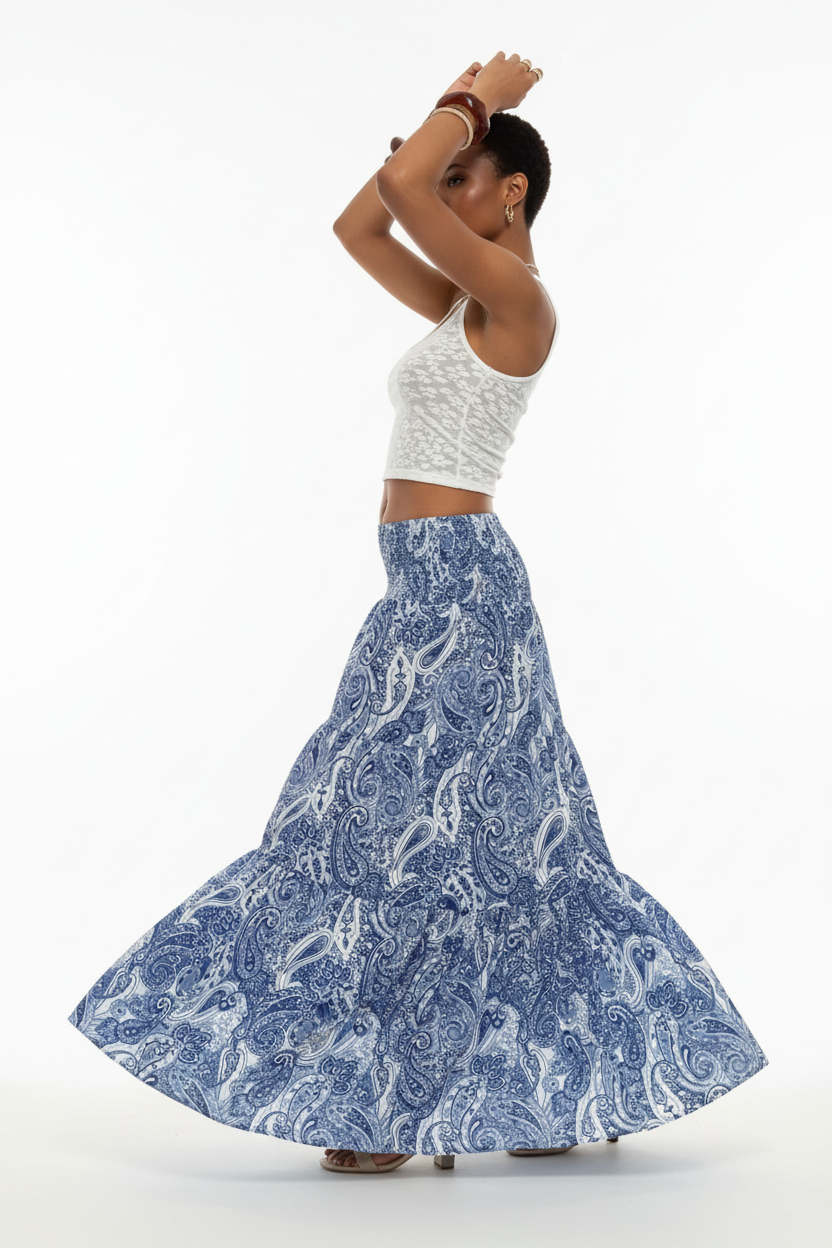 Jupe longue bohème Black-Coat bleue et blanche à imprimé paisley avec taille smockée et volants étagés - profil latéral complet d'une mannequin en mouvement gracieux sur fond blanc studio, soulignant le mouvement fluide des volants, la silhouette bohème romantique, l'imprimé paisley bleu et blanc et la taille smockée confortable