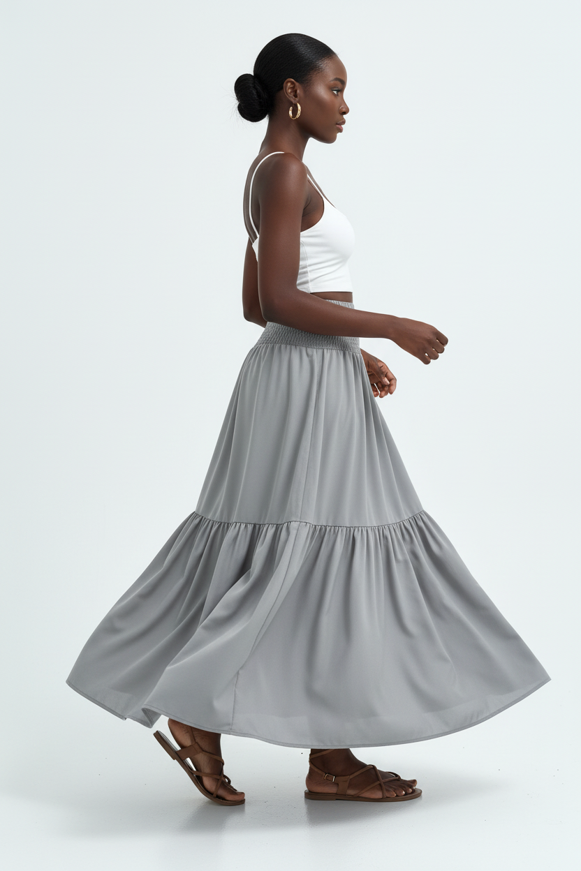 Jupe longue smockée à volants Black-Coat grise - profil latéral complet d'une mannequin en mouvement gracieux sur fond blanc studio, soulignant le mouvement fluide du volant étagé, la silhouette élégante et décontractée, la taille smockée confortable et le tombé parfait du tissu léger