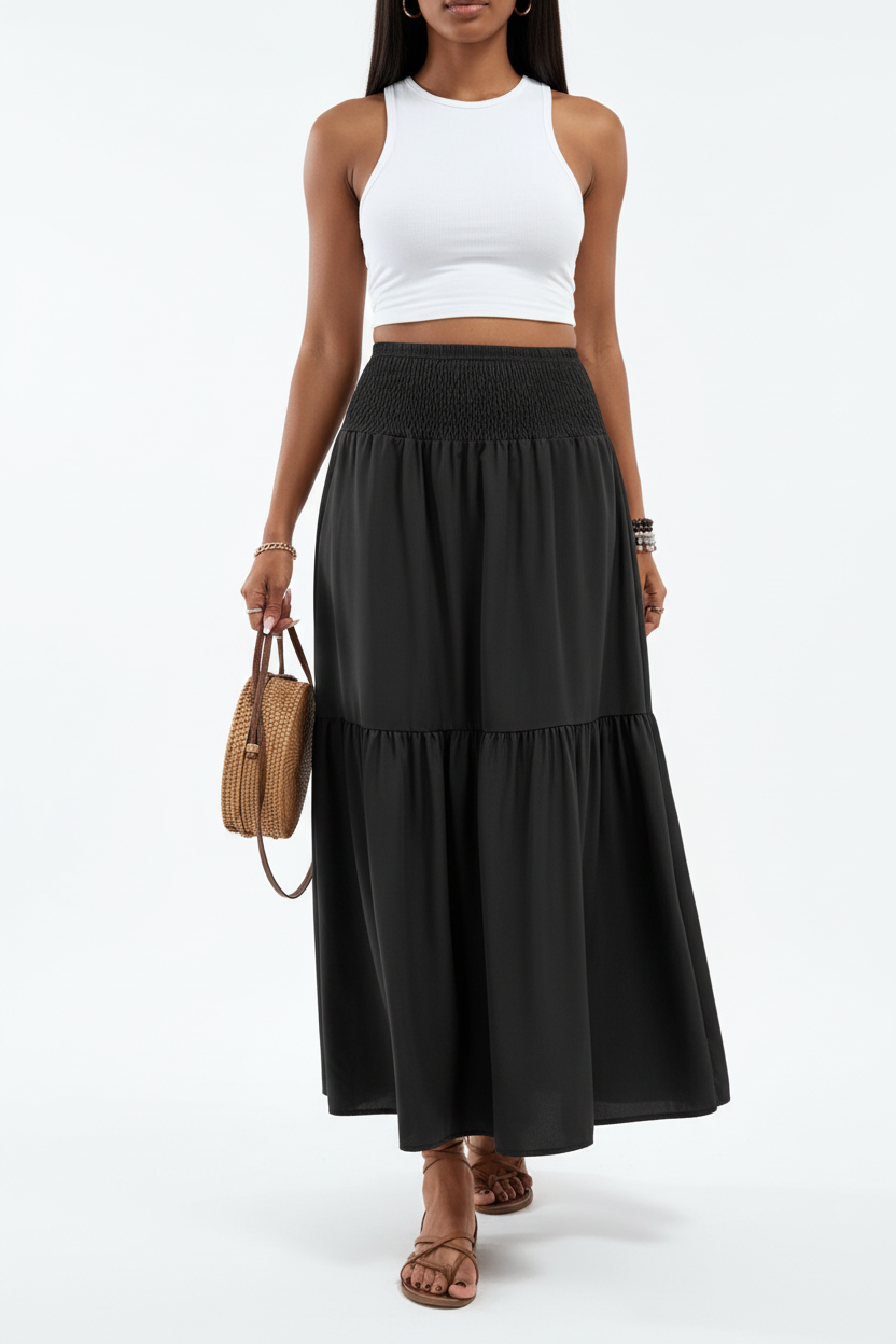 Jupe longue smockée à volants Black-Coat noire - vue de face frontale complète d'une mannequin en pose debout sur fond blanc studio, présentant la taille smockée ultra-confortable, le volant étagé en bas qui ajoute du mouvement, la longueur maxi fluide et élégante et la silhouette minimaliste chic
