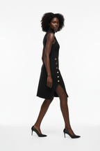 Robe mini col montant Black-Coat avec boutons dorés - vue arrière trois-quarts d'une mannequin en rotation douce sur fond blanc studio, dévoilant la fente latérale avec boutons dorés vue de côté, la coupe ajustée qui sculpte la silhouette et le mouvement élégant de la robe structurée