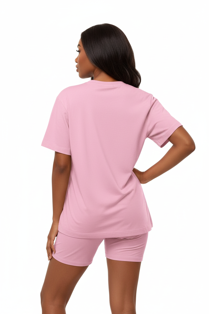 Mannequin en pose assurée main sur la hanche portant l'ensemble coordonné t-shirt oversize et short cycliste rose Black-Coat, vue trois-quarts — coloris rose doux et féminin apportant fraîcheur et bonne humeur, t-shirt oversize col rond au tombé parfait, manches courtes structurées, short cycliste gainant mettant en valeur la silhouette, ensemble monochrome élégant et moderne, fond blanc, photographie mode éditoriale contemporaine Black-Coat, de la salle de sport à la terrasse du café
