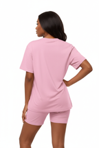 Mannequin en pose assurée main sur la hanche portant l'ensemble coordonné t-shirt oversize et short cycliste rose Black-Coat, vue trois-quarts — coloris rose doux et féminin apportant fraîcheur et bonne humeur, t-shirt oversize col rond au tombé parfait, manches courtes structurées, short cycliste gainant mettant en valeur la silhouette, ensemble monochrome élégant et moderne, fond blanc, photographie mode éditoriale contemporaine Black-Coat, de la salle de sport à la terrasse du café

