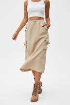 Jupe cargo beige mi-longue avec multiples poches latérales - pose dynamique en mouvement révélant la fluidité et l'amplitude de la jupe utilitaire - BLACK-COAT