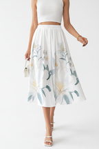 Jupe midi imprimé floral blanc boutonnée - vue de face montrant mannequin en mouvement de marche naturelle avec motif floral délicat pastel et feuilles vertes détails boutons décoratifs taille élastique silhouette A-line fluide et longueur midi - BLACK0COAT