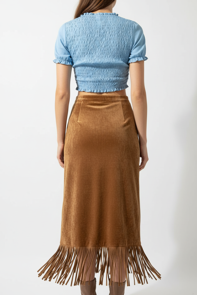 "Jupe midi velours camel avec franges - vue arrière dos montrant la coupe ajustée de la jupe velours camel, les franges décoratives marron à l'ourlet vues de dos, texture velours luxueuse, mannequin en crop top bleu ciel, fond blanc studio BLACK-COAT"