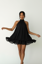 Robe mini halter Black-Coat à double volant - vue corps entier d'une mannequin avec bras légèrement étendus sur fond blanc studio, illustrant le tombé parfait du tissu 100% polyester, la longueur mini flatteuse, le col halter qui allonge la silhouette et les deux étages de volants qui ajoutent du volume et du mouvement
