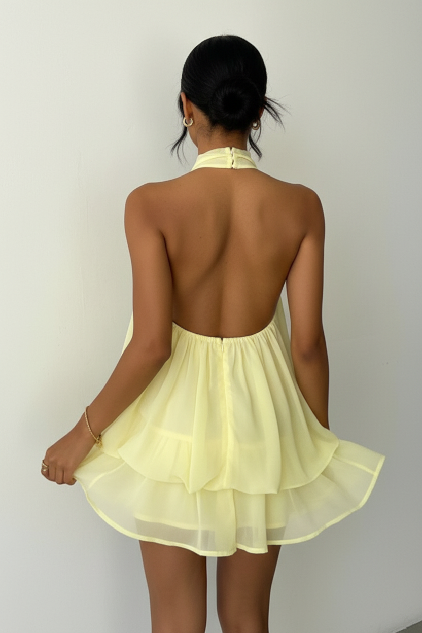 Robe mini halter Black-Coat jaune pâle avec volants superposés - vue arrière complète d'une mannequin sur fond blanc studio, dévoilant les détails de la construction arrière avec attache au cou, le dos nu sophistiqué, la jupe à double volant vue de dos et la teinte jaune douce et lumineuse du tissu polyester

