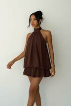 Robe mini halter Black-Coat marron chocolat avec volants superposés - vue de face frontale complète d'une mannequin en pose debout sur fond blanc studio, présentant le col halter montant sophistiqué, le décolleté élégant, les deux étages de volants qui créent du volume et du mouvement, et la teinte marron riche et chaleureuse du tissu 100% polyester
