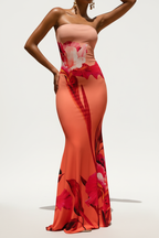 "Robe maxi bodycon bustier imprimé floral corail rouge - pose décontractée naturelle montrant l'élégance estivale de la tenue, décolleté bustier bandeau, imprimé floral audacieux vibrant, silhouette moulante, style vacances chic, fond blanc studio BLACK-COAT"