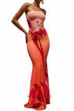 "Robe maxi bodycon bustier imprimé floral corail rouge - vue trois-quarts face angle montrant la profondeur et dimension de la robe, décolleté bustier bandeau, imprimé floral vibrant audacieux grandes fleurs rouges roses sur dégradé corail orange, silhouette bodycon, fond blanc studio BLACK-COAT"