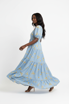 : Robe Maxi Étagée à Imprimé Marguerites Black-Coat bleu clair - vue trois-quarts en mouvement révélant les volants étagés et l'imprimé floral champêtre