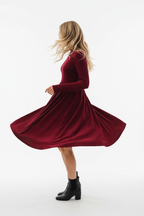 "Robe mini velours bordeaux col volant - en mouvement twirl montrant la jupe mini évasée qui tourne et s'ouvre, tissu velours fluide en mouvement dynamique, col à volants, texture bordeaux riche, fond blanc studio BLACK-COAT"