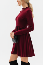 "Robe mini velours bordeaux col volant - vue de profil latéral montrant la silhouette ajustée évasée, col à volants visible de côté, jupe mini ligne A fluide, texture velours riche bordeaux, fond blanc studio BLACK-COAT"